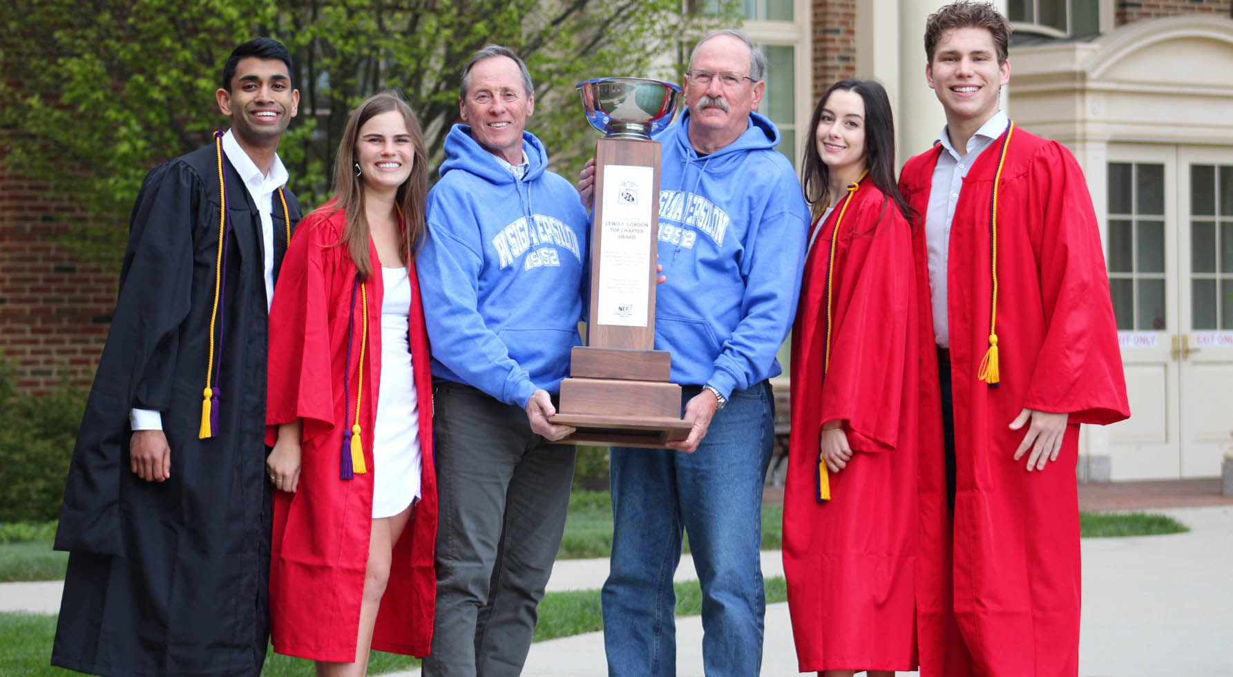 Graduates and leaders holding a large trophy