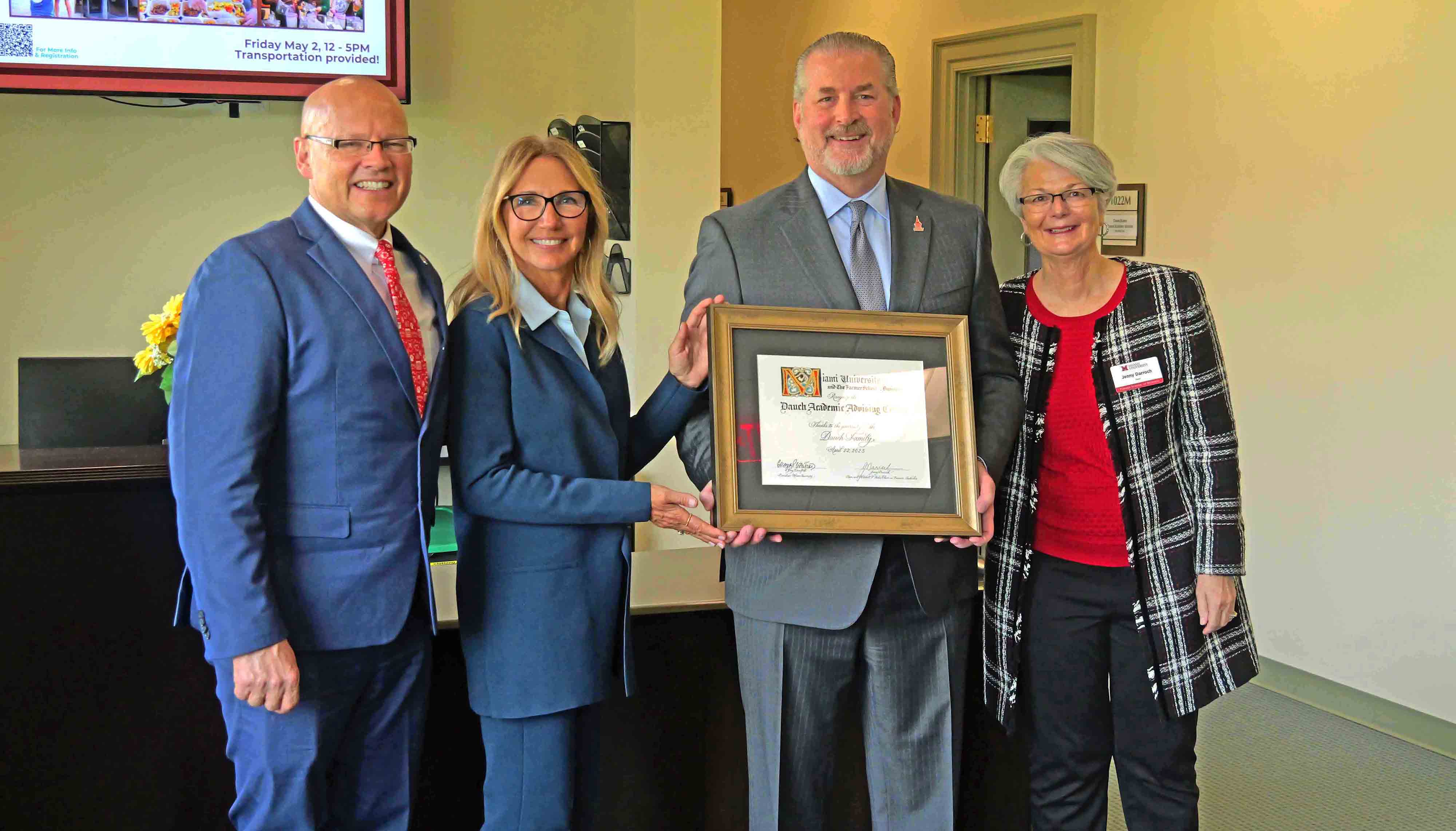 David Dauch, Anita Dauch, Gregory Crawford, and Jenny Darroch posing for a photo while holding a framed certificate in a welcoming office environment.