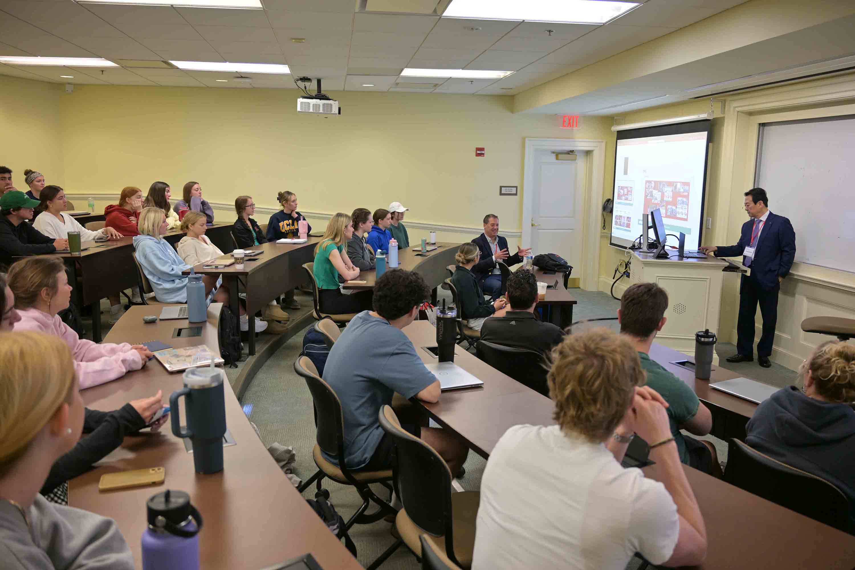 A professional presentation in a classroom setting, with a speaker addressing an attentive audience of students and faculty.