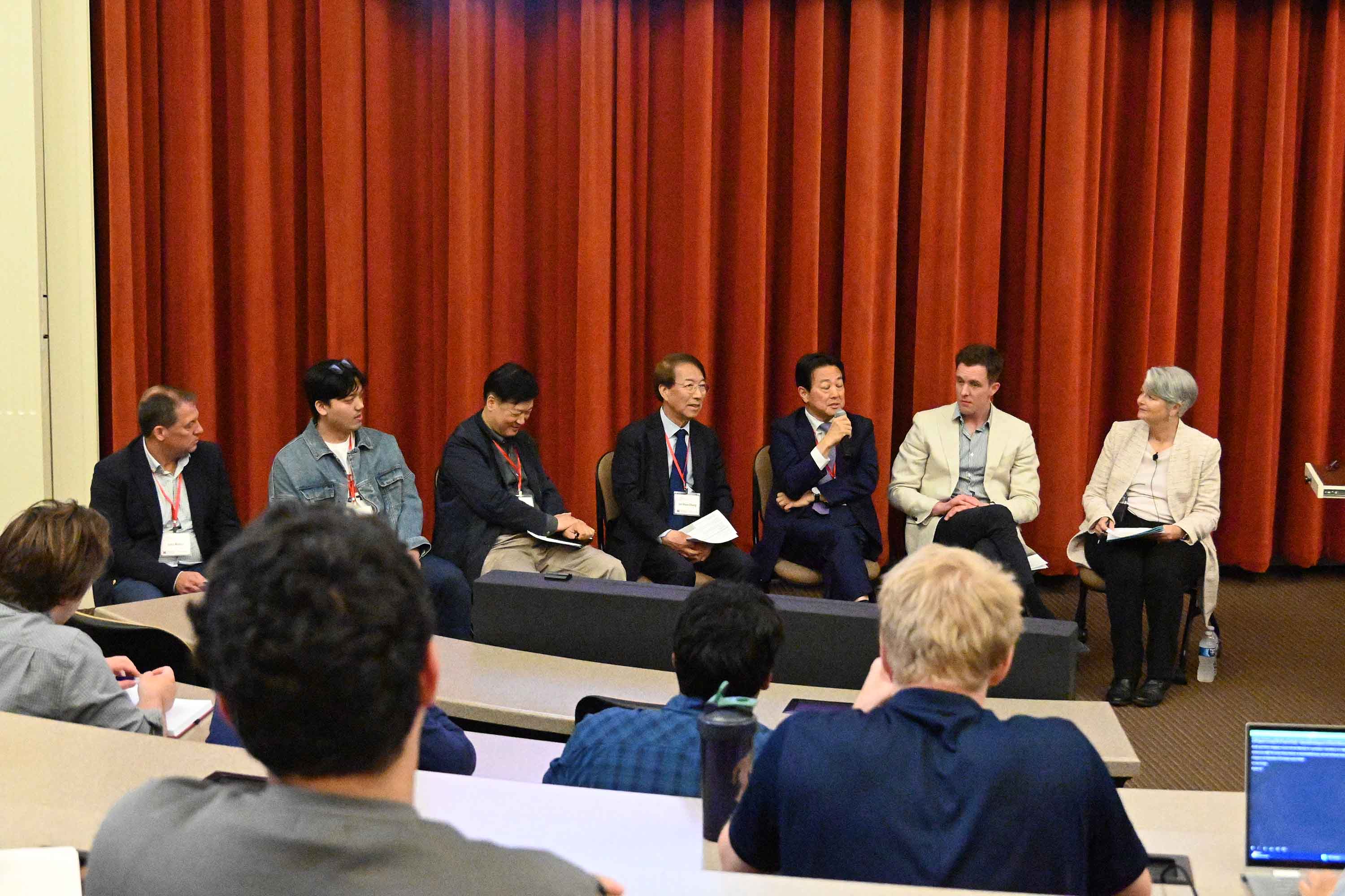 Panel discussion featuring several speakers on stage at a conference, with an audience visible in the foreground.