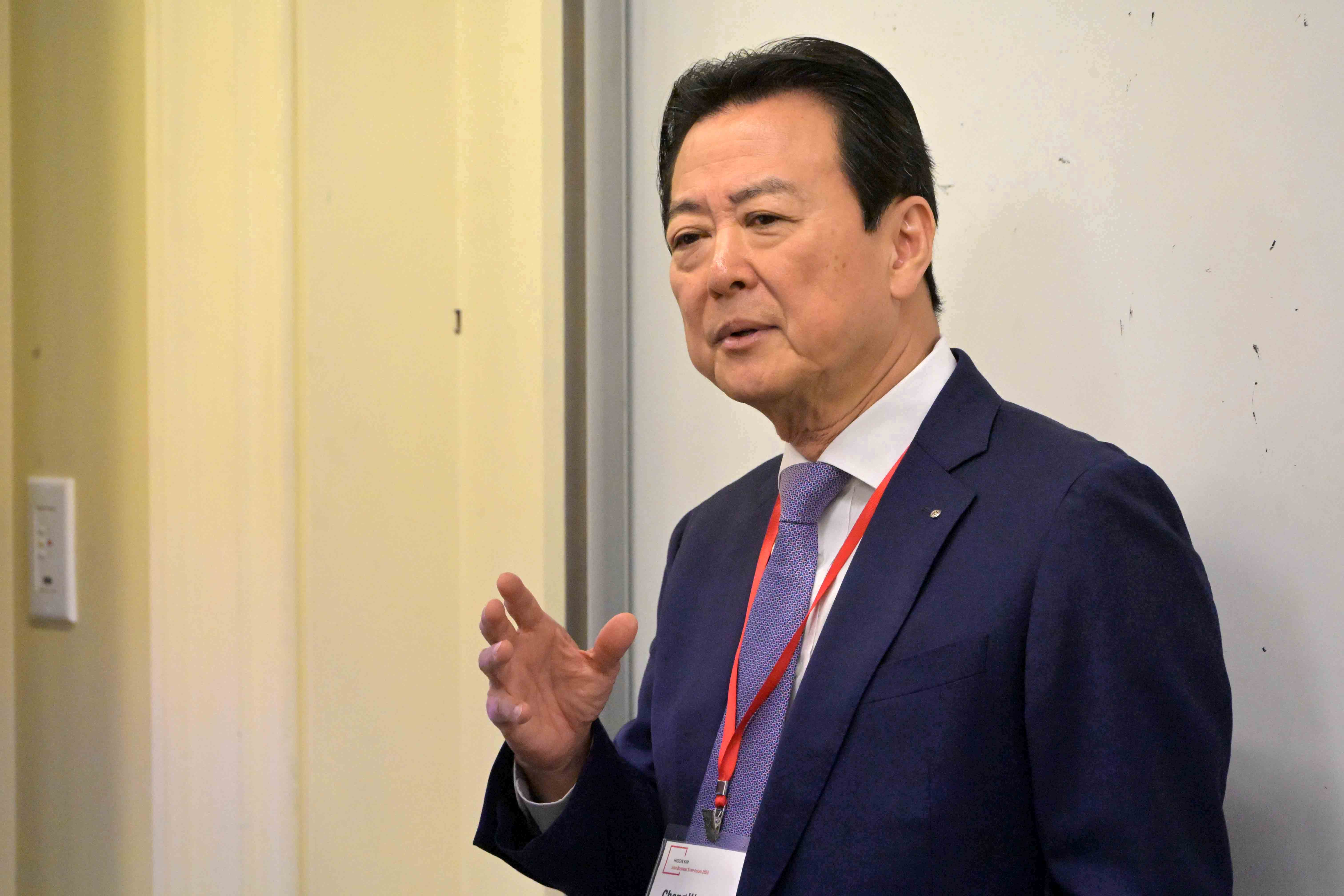 A Higgin Kim presenter presenting in a business setting, wearing a suit and a name badge.