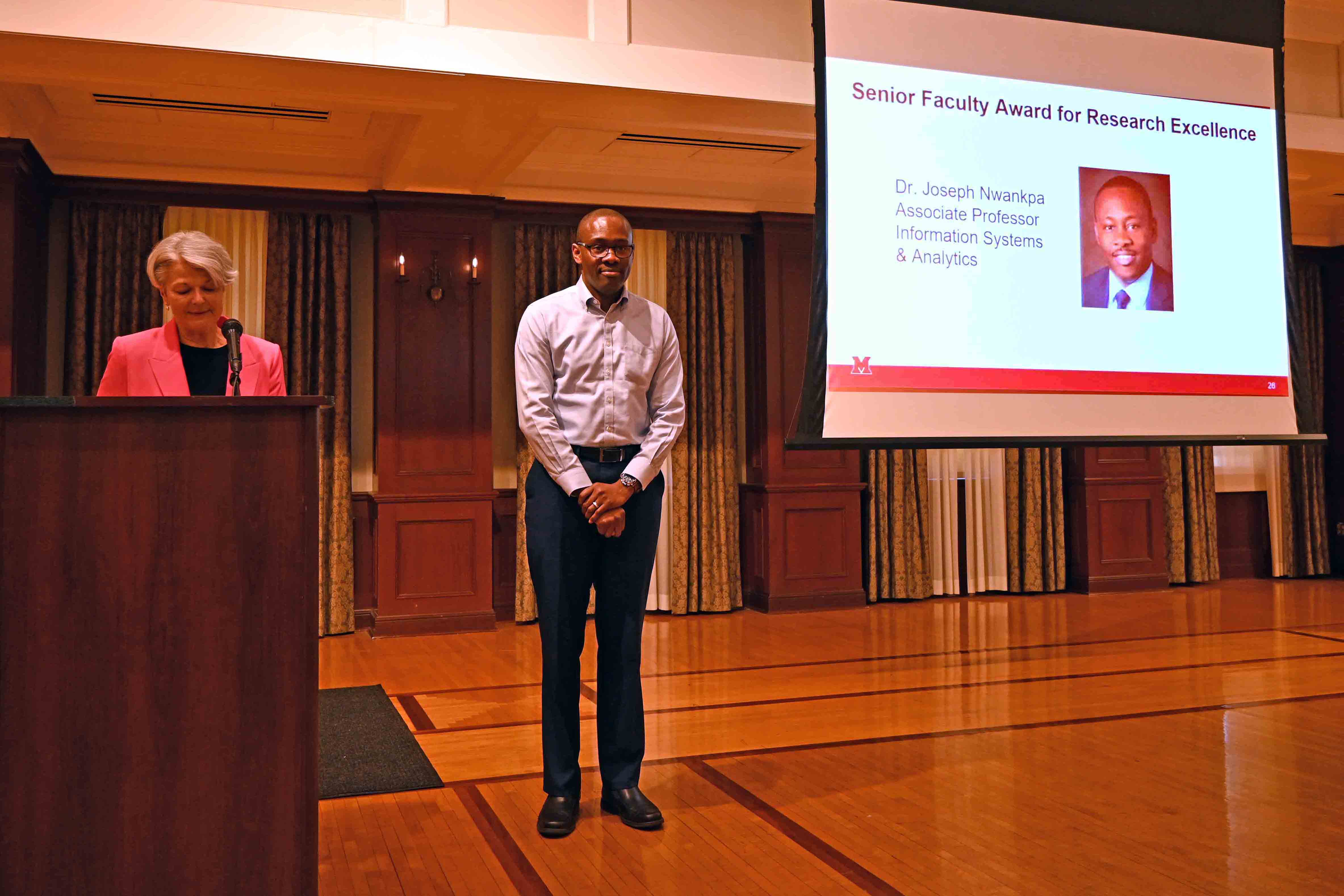Joseph Nwankpa listens as dean Jenny Darroch describes the award he's receiving