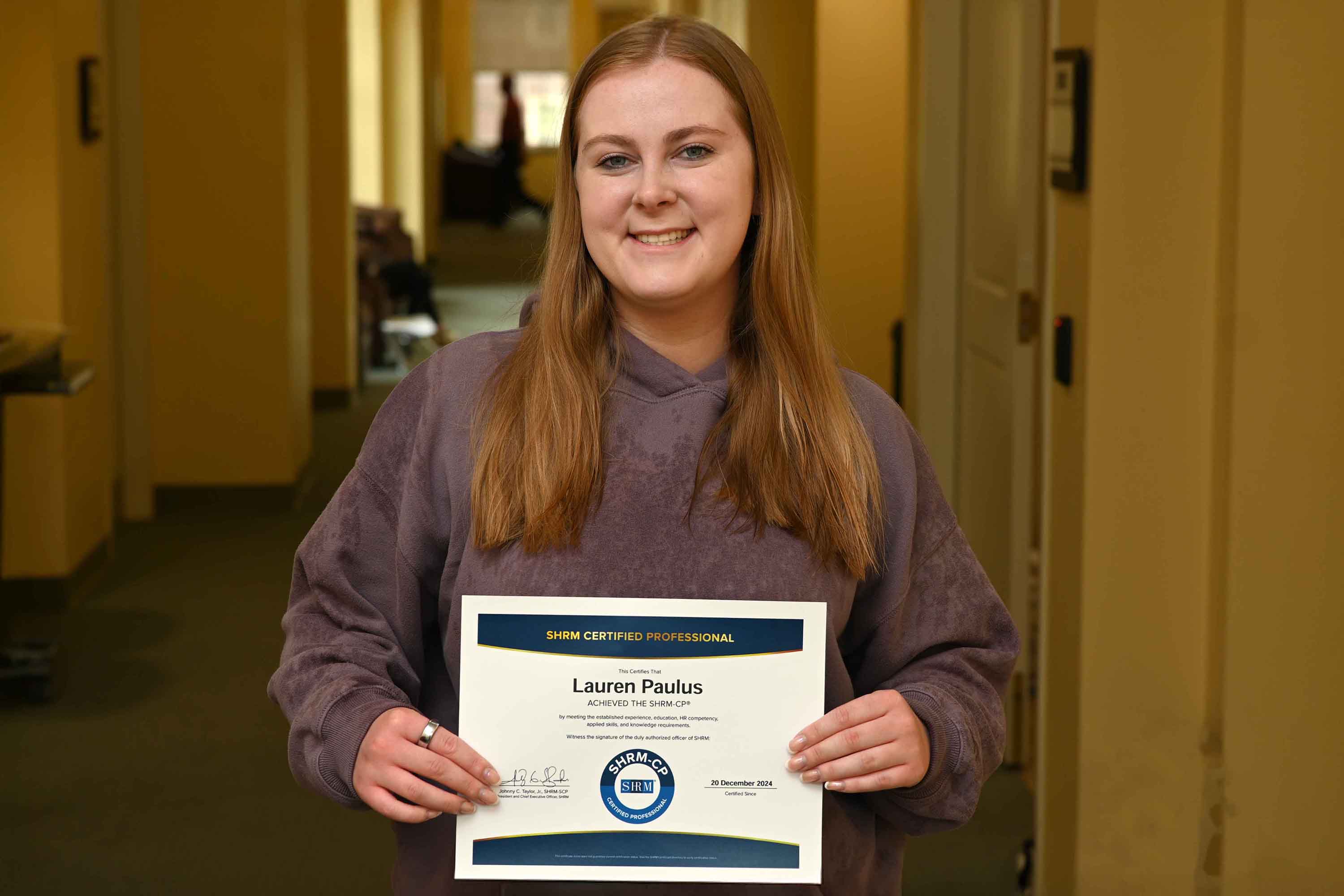 Lauren Paulus holds a certification diploma proudly, showcasing her achievement as a SHRM Certified Professional.