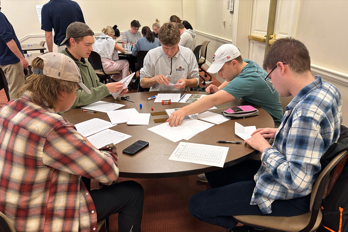 A group of five students collaborates around a table, engaging in hands-on activities involving paper and tools.