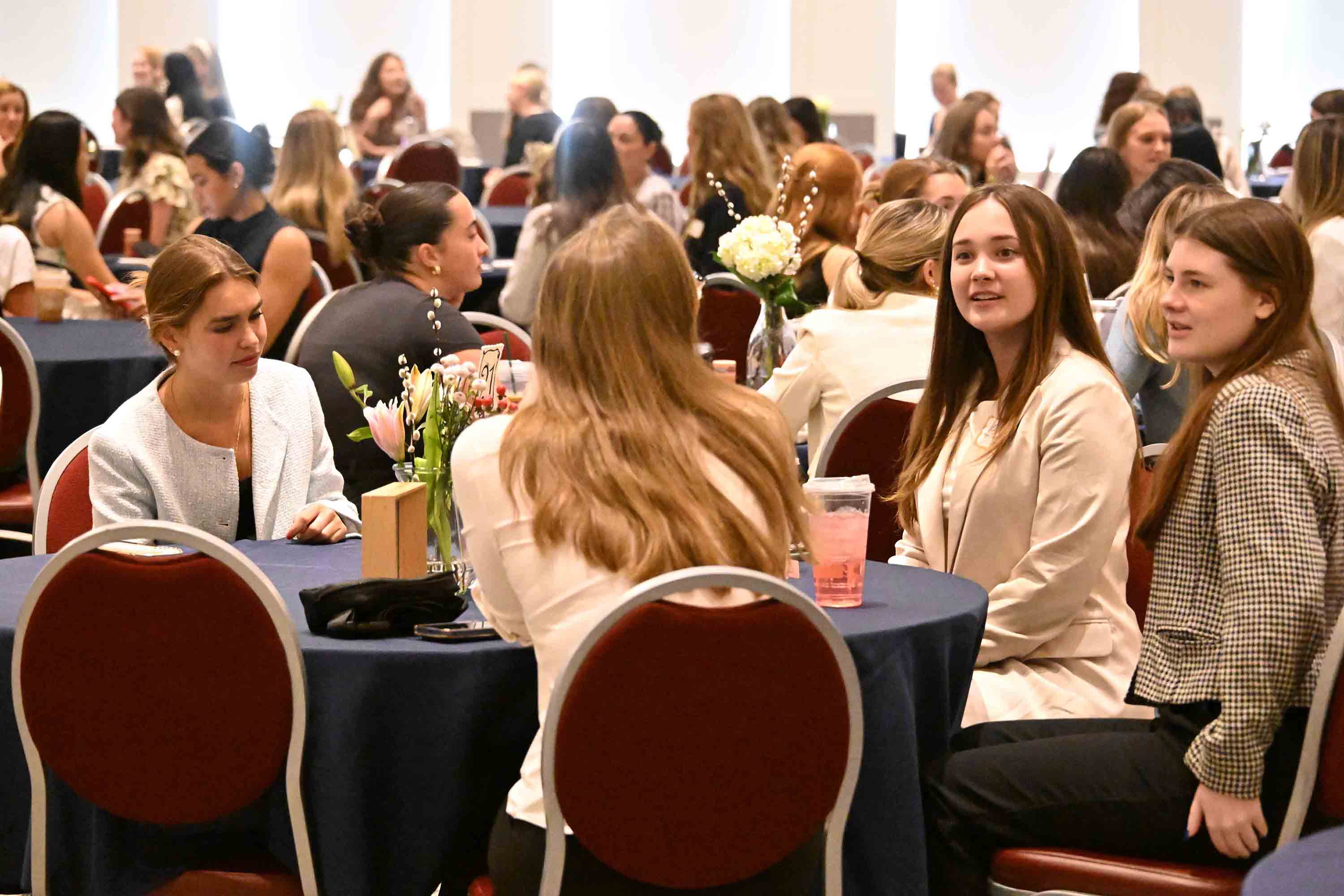 A group of students engaged in conversation around round tables at a conference or networking event.