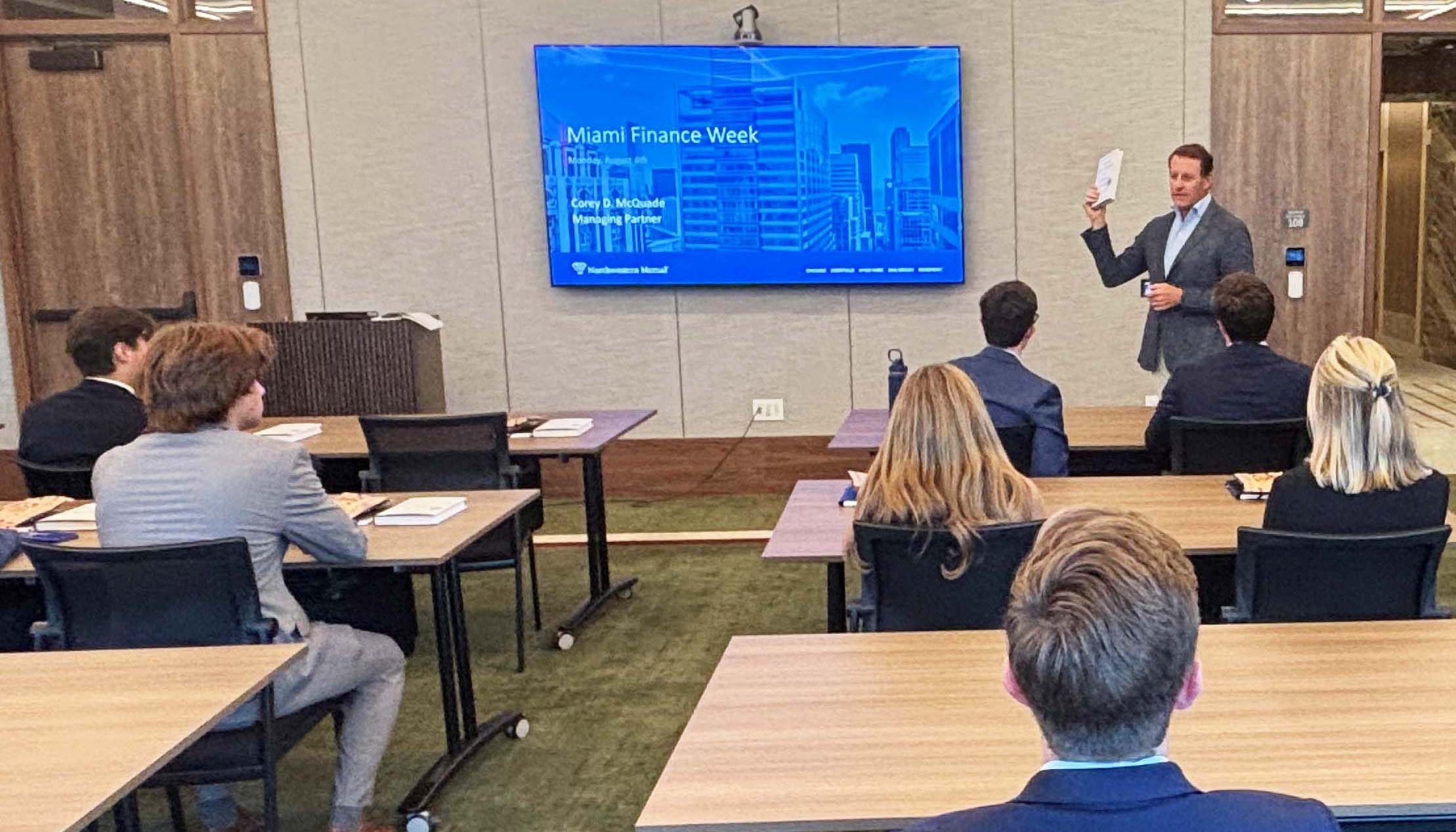 A professional presentation during Miami Finance Week, featuring a speaker addressing an audience in a conference room.