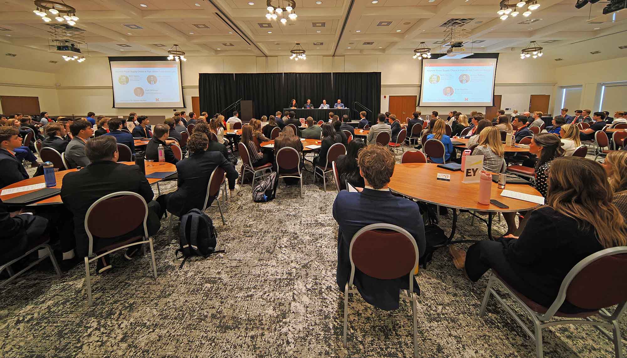 Wide shot of front of room at roundtable, with four speakers on the platform