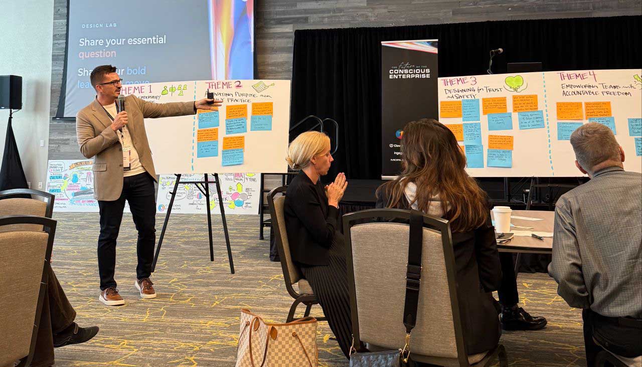 A speaker presents ideas during a workshop, with participants engaged and discussion boards displaying themes and insights.