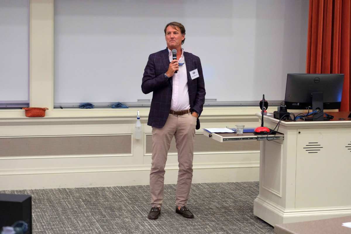 Dick Williams addressing an audience with a microphone in hand during a presentation.