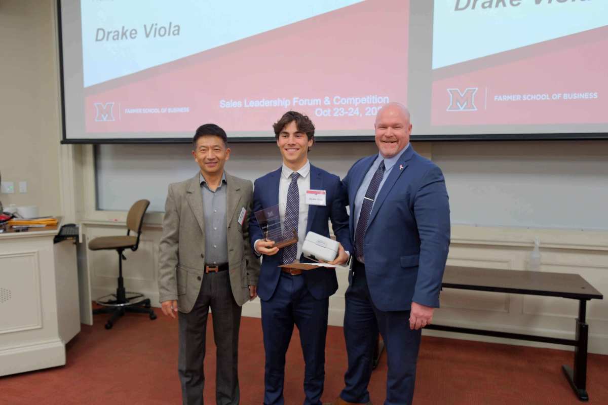 Drake Viola stands with two men, holding an award and a virtual reality headset, during the Sales Leadership Forum & Competition at the Farmer School of Business.
