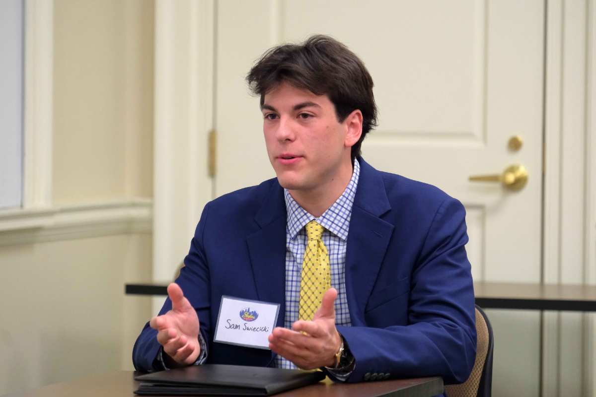 A young man in a blue suit and yellow tie engages in discussion at a formal meeting.