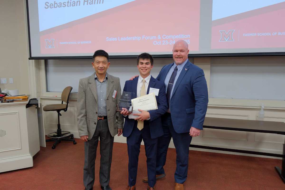 Three men stand together in a conference room after a Sales Leadership Forum, with one holding a certificate and award. The backdrop features event branding from the Farmer School of Business.