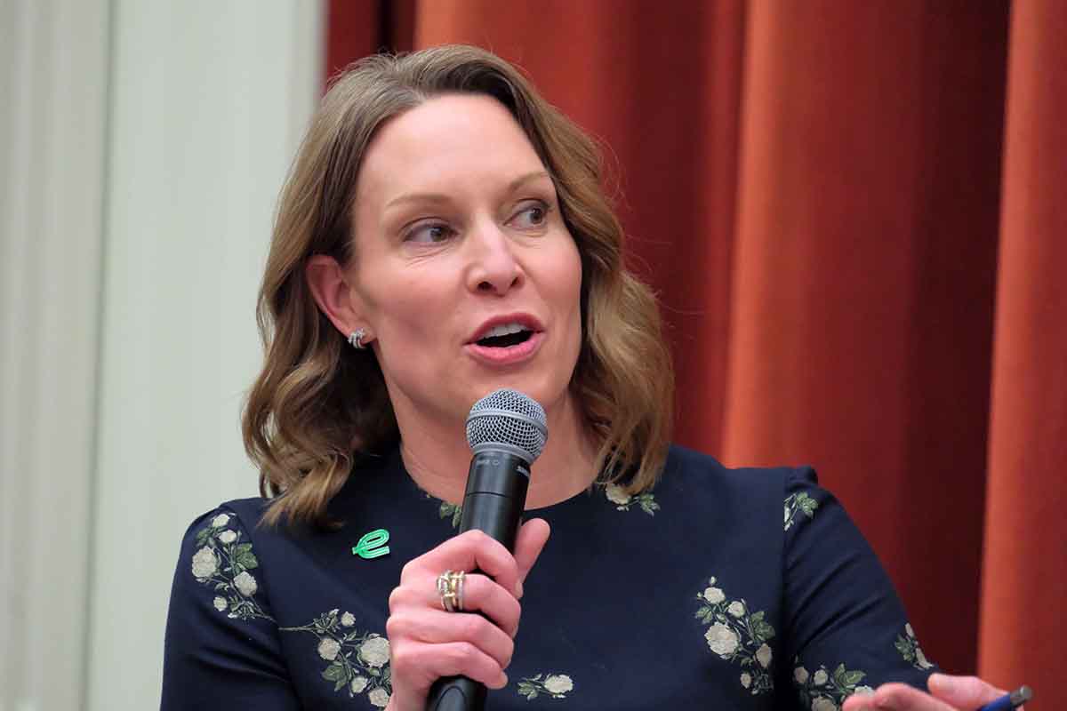 A woman speaking into a microphone, wearing a floral dress and earrings, during a panel discussion.