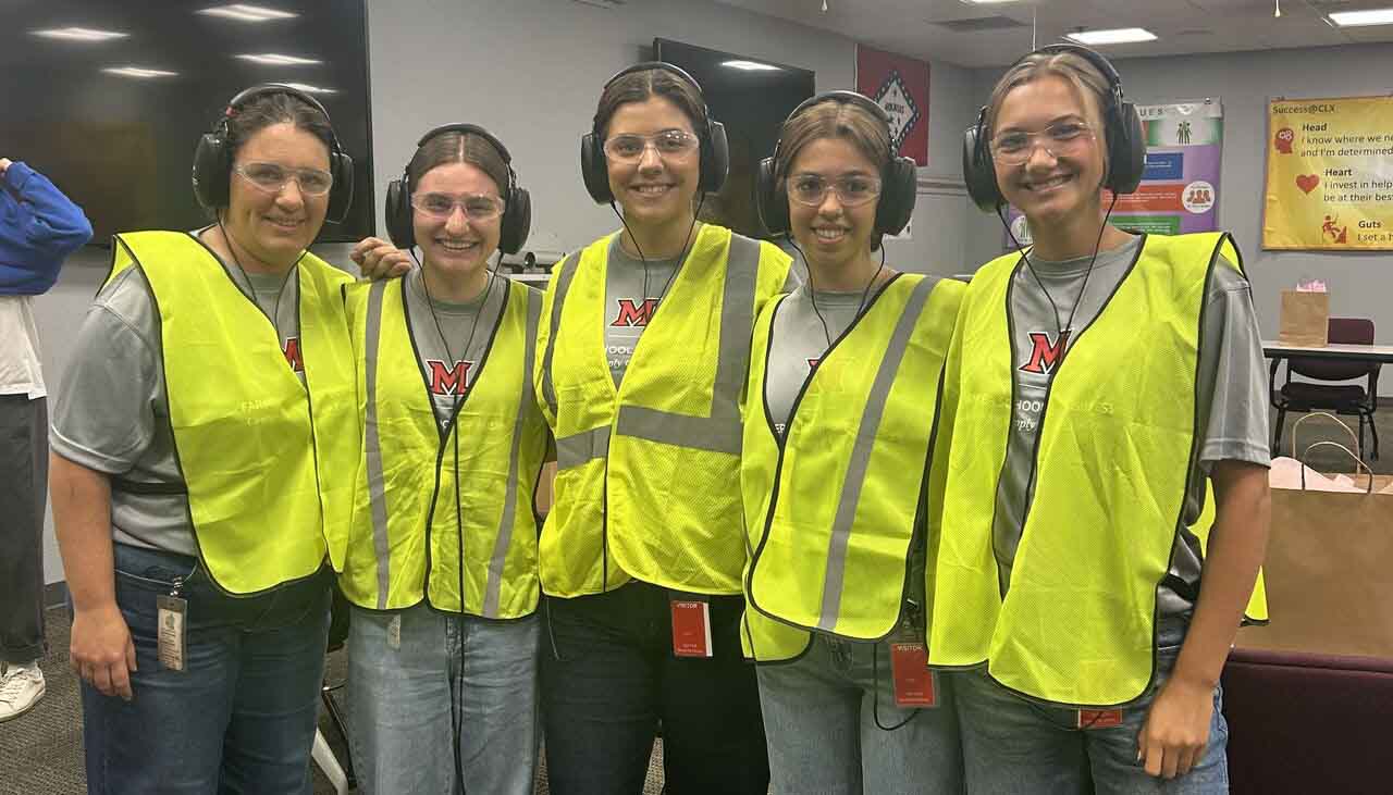 Murfield and students wearing safety vests and headphones, posing together in a classroom setting.