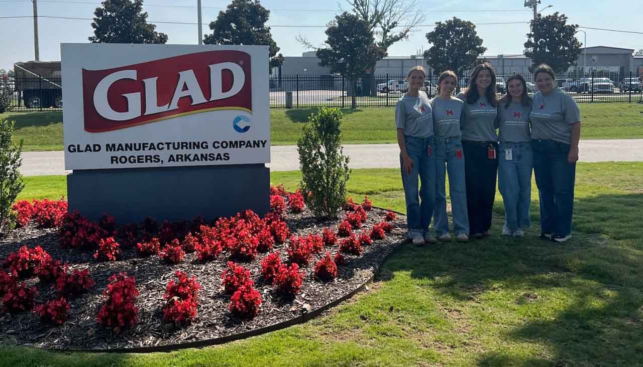 GLAD Manufacturing Company sign in Rogers, Arkansas, with Murfield and students posing in front of it.