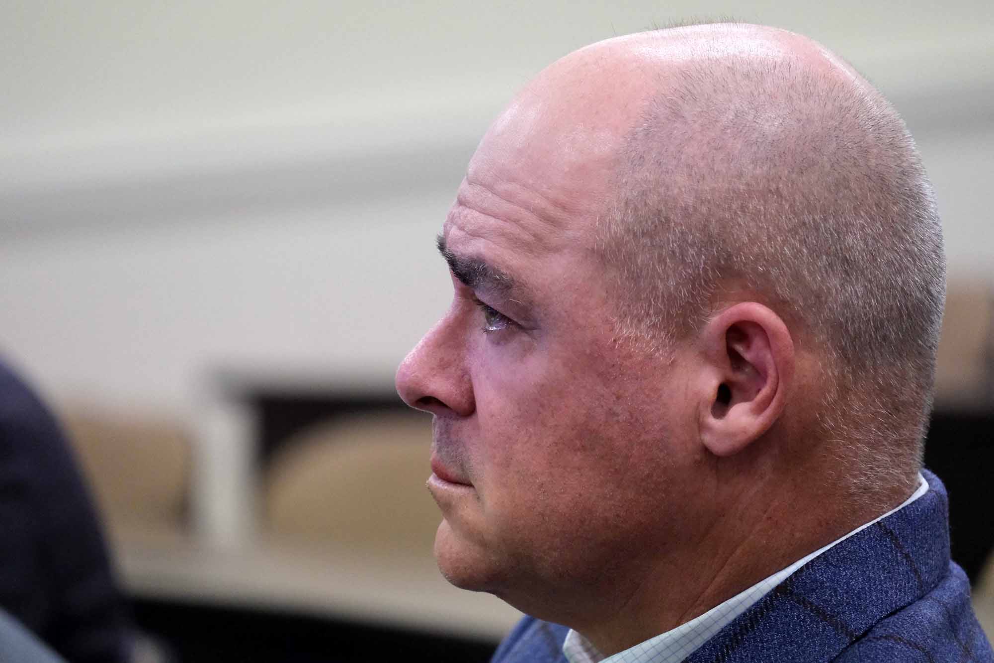 A man with a closely shaved head looks pensive during a meeting.