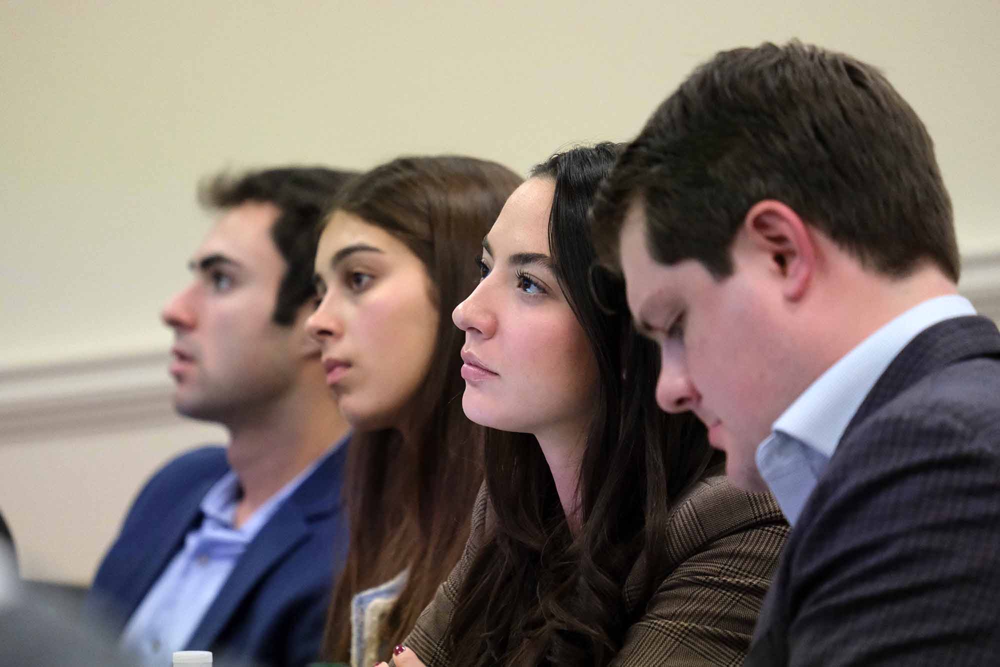 A diverse group of young adults engaged in discussion, focused on a presentation in a professional setting.
