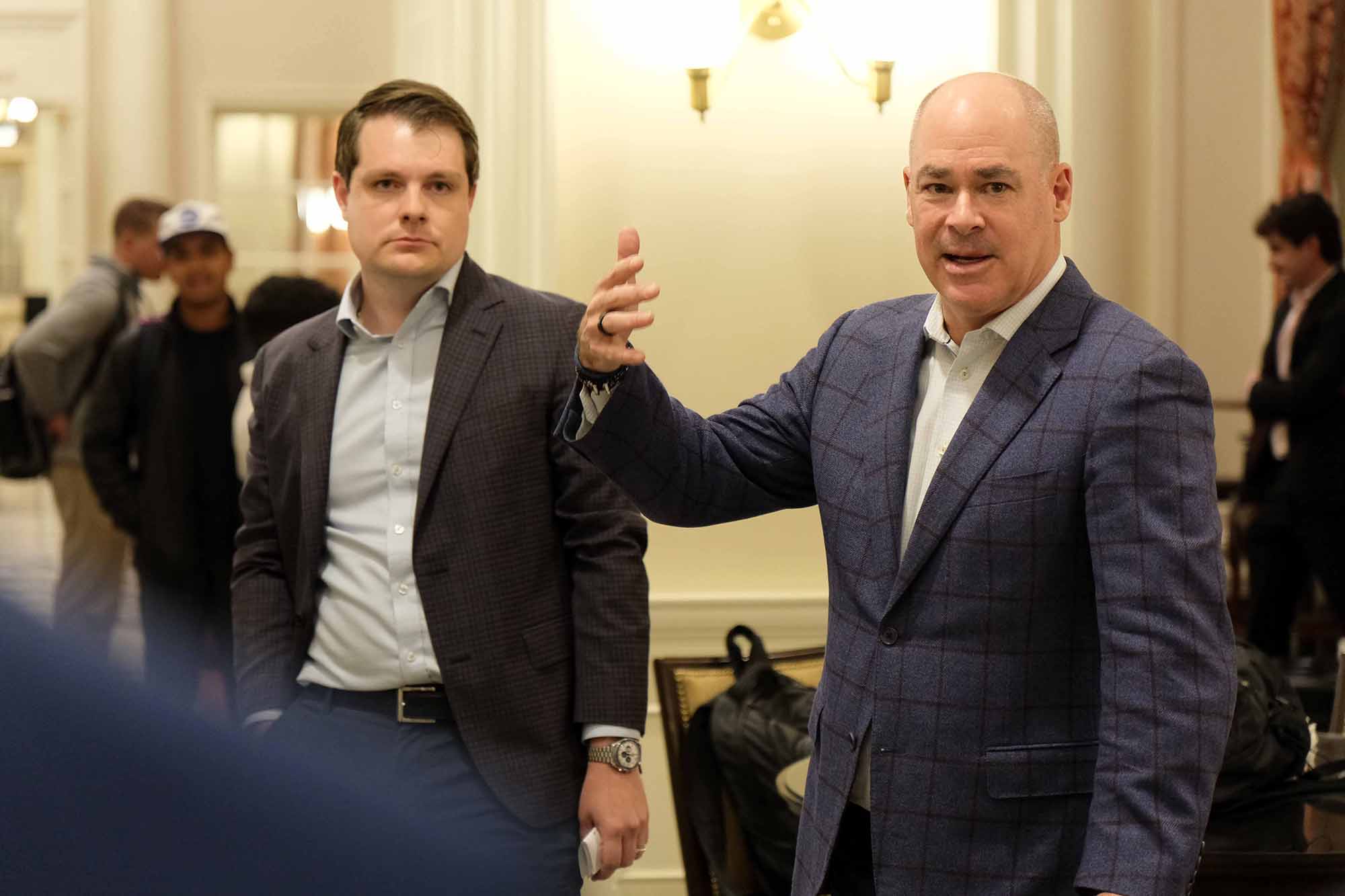 Two men engaged in a discussion in a formal setting, with one gesturing while speaking and the other listening attentively.