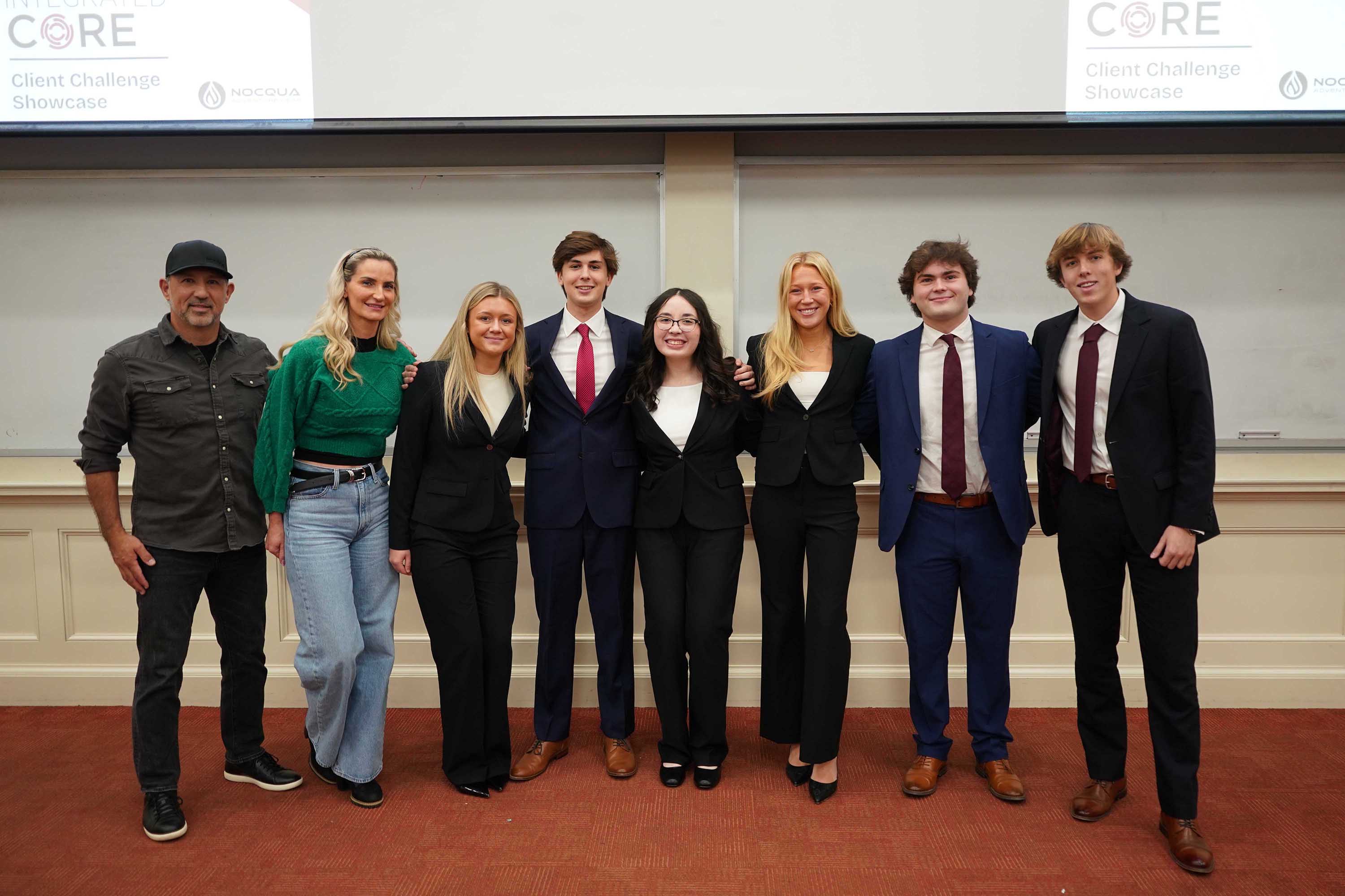Group photo of participants and judges at the Client Challenge Showcase, featuring seven individuals in business attire.