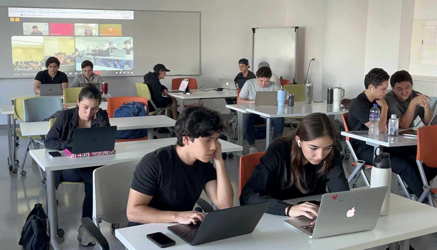 Monterrey students engaged in a collaborative learning environment, working on laptops at desks in a classroom setting.