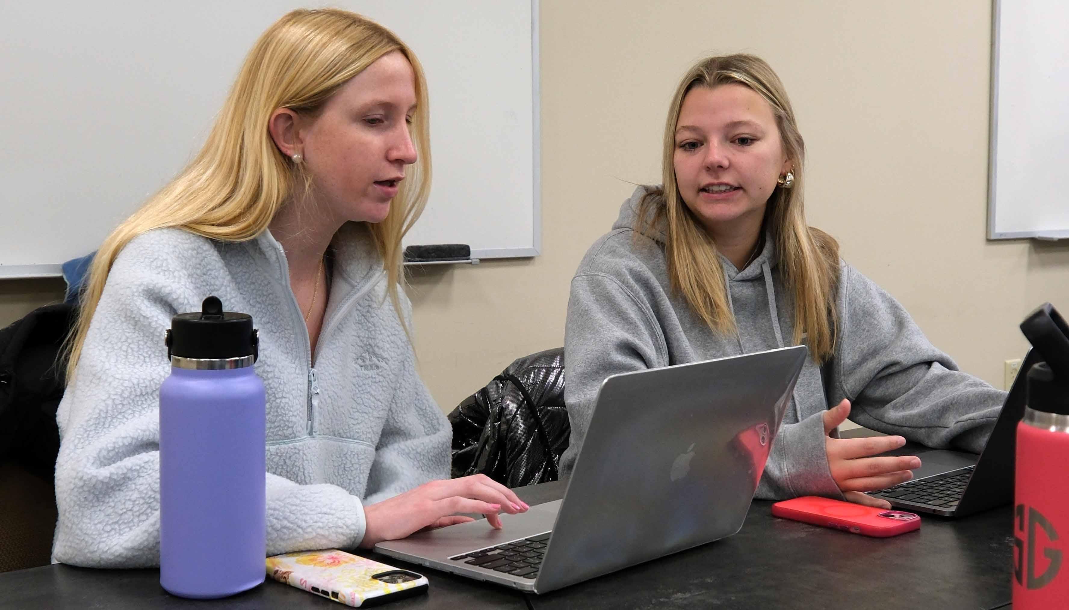 Two students collaborating on a laptop during a study session, with water bottles and personal items on the table.