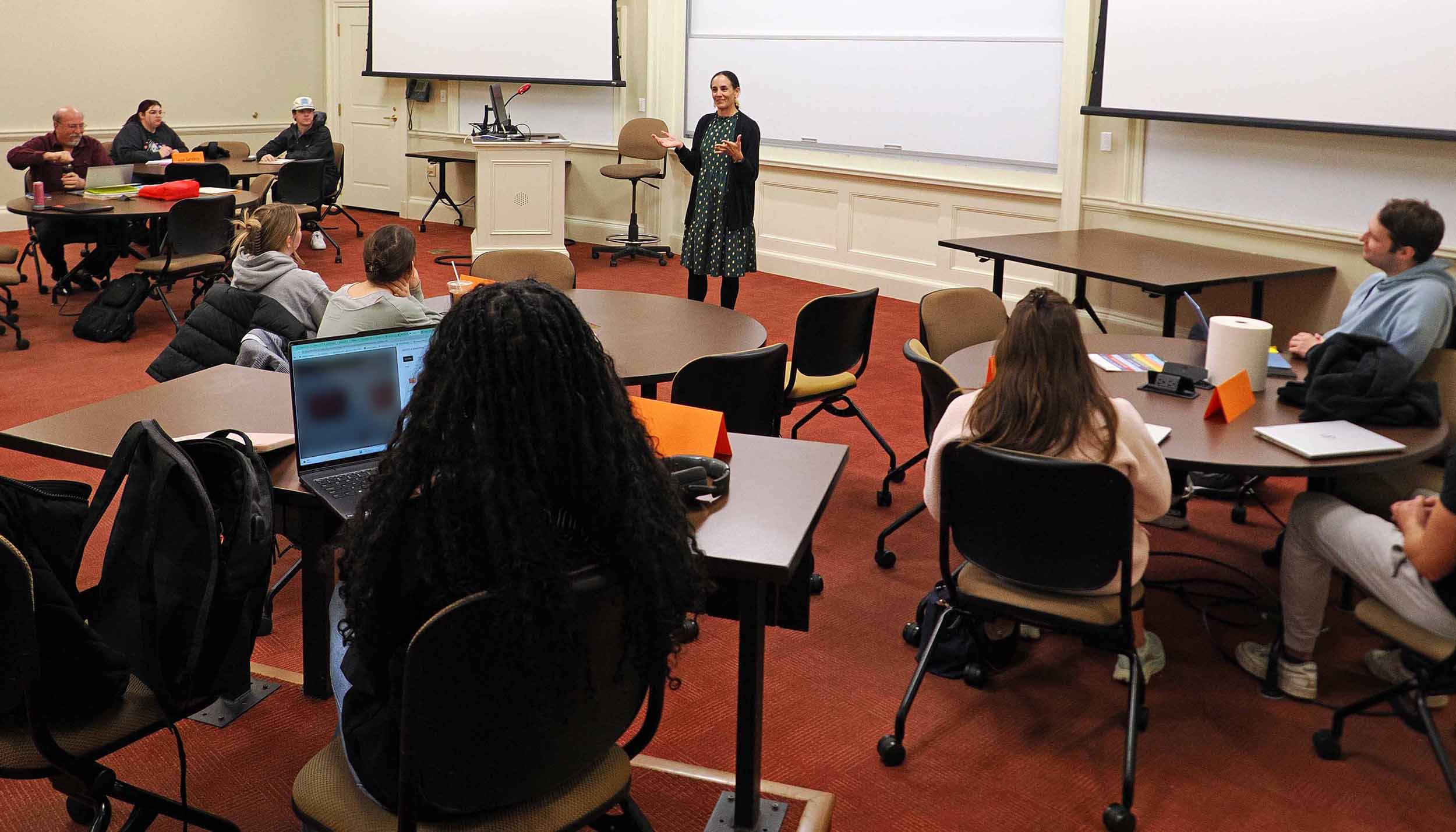 Palatka speaking to students seated at round tables in a classroom.