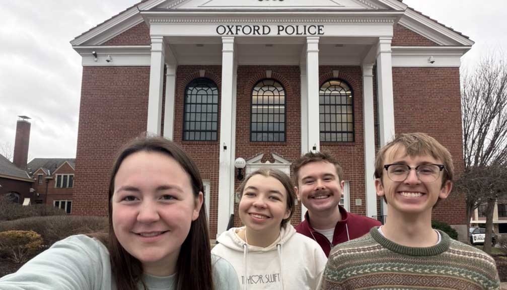 Four smiling people posing in front of the Oxford Police building.
