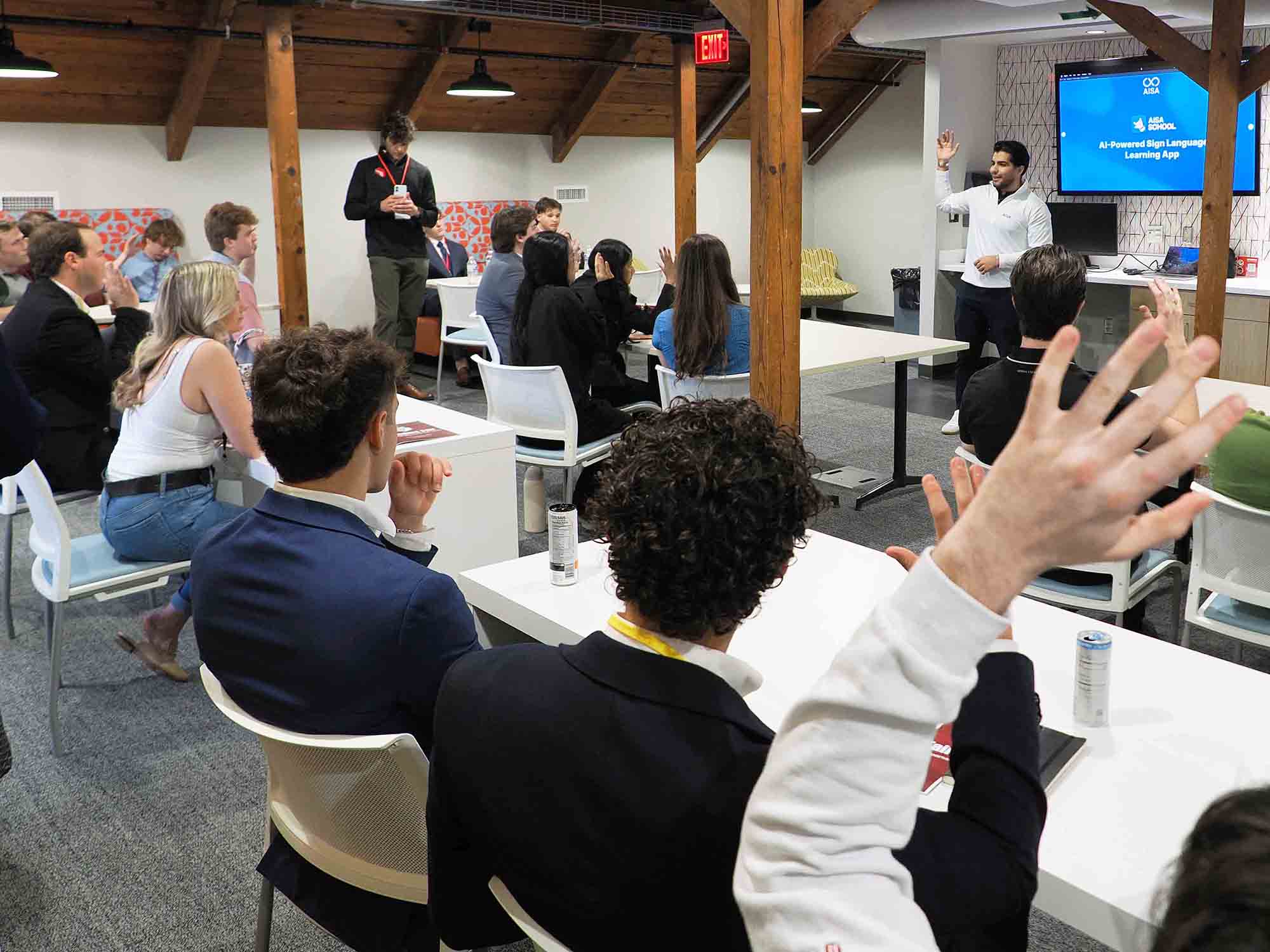 Presenter leading a workshop as audience members raise their hands in a classroom setting.