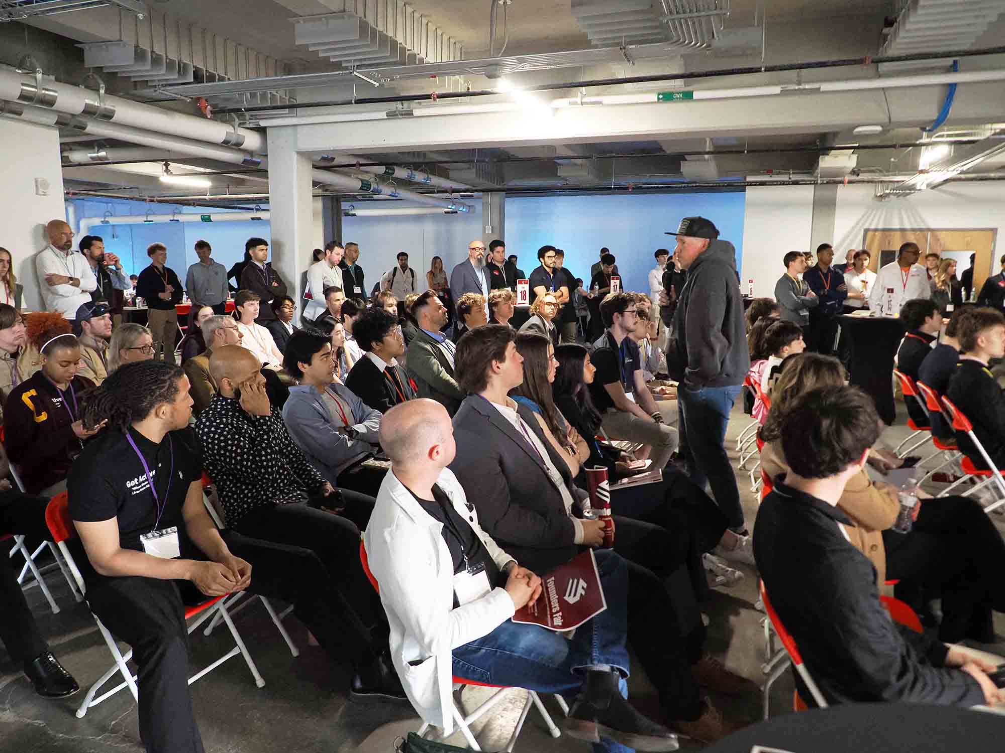 Audience seated at an indoor networking or demo event while a presenter speaks.