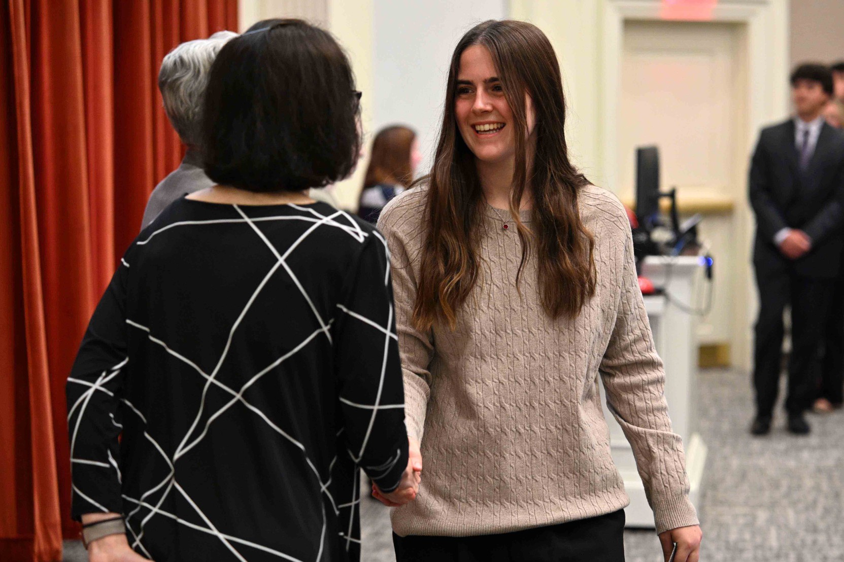 Woman smiling as she shakes hands with another person at an indoor event.