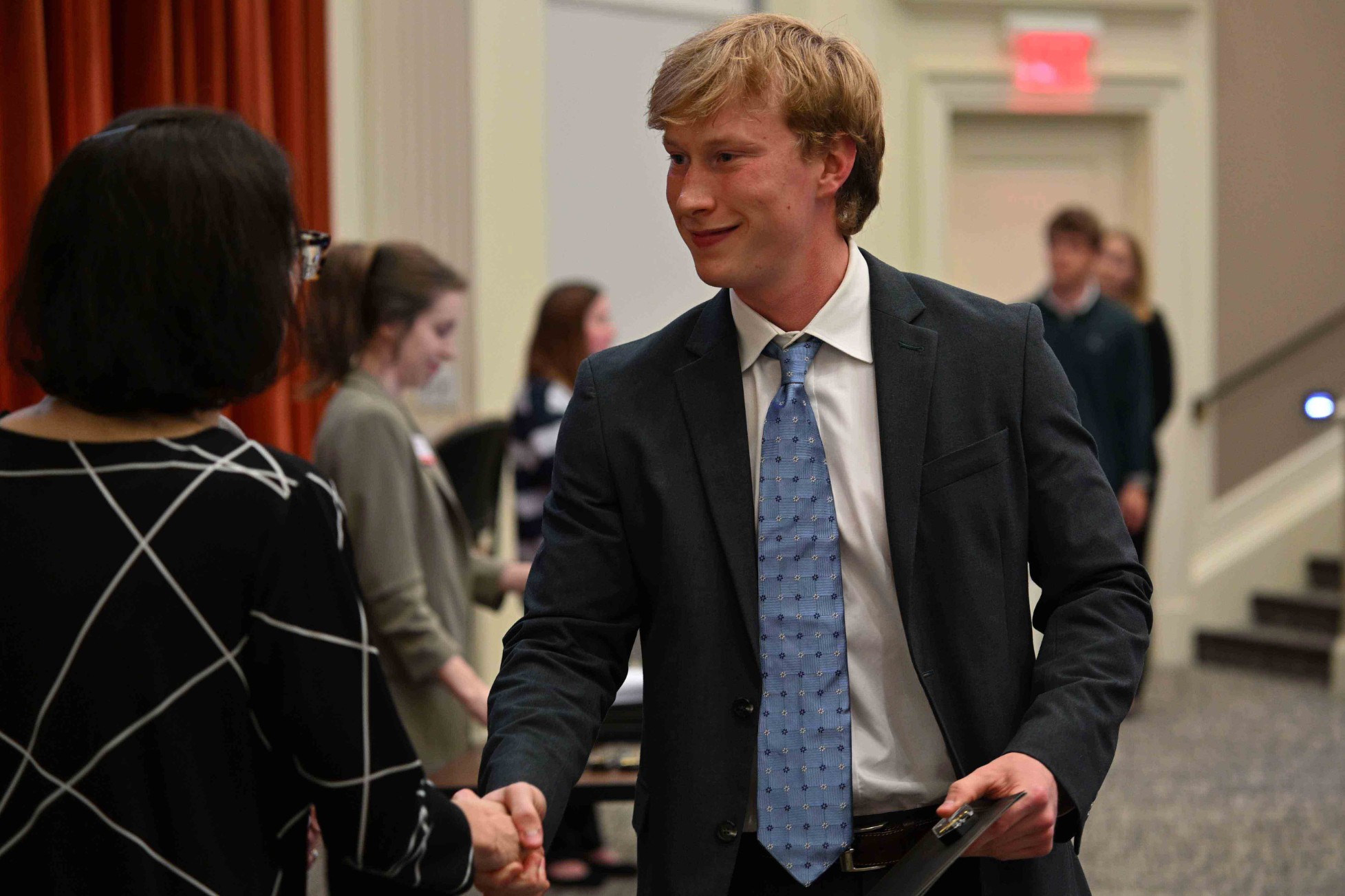Young man in a suit shakes hands with a woman at a networking event.