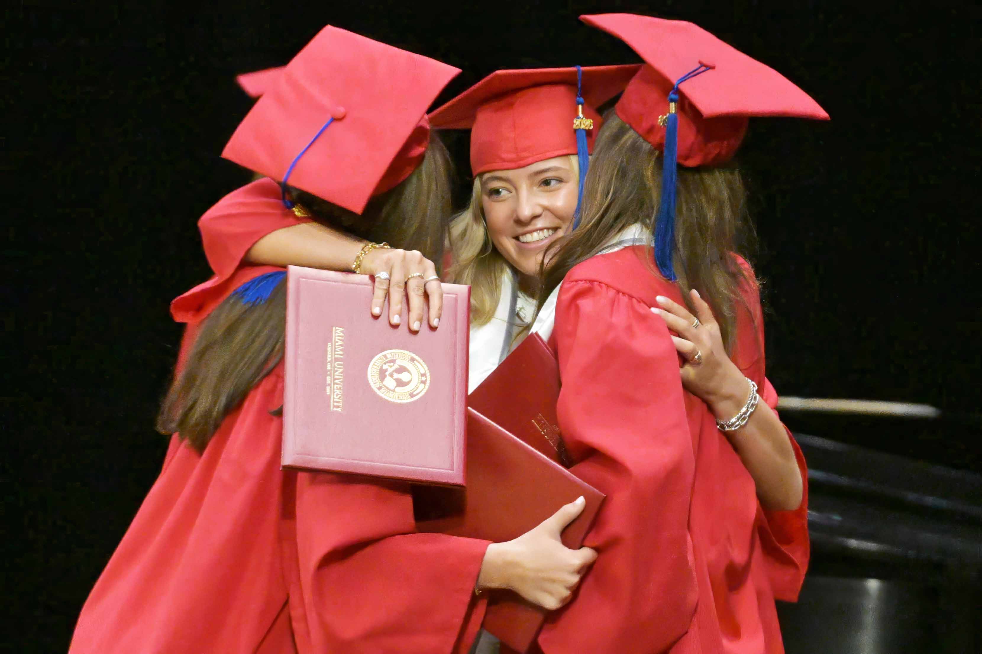 Student being hugged by two other students after receiving her diploma cover