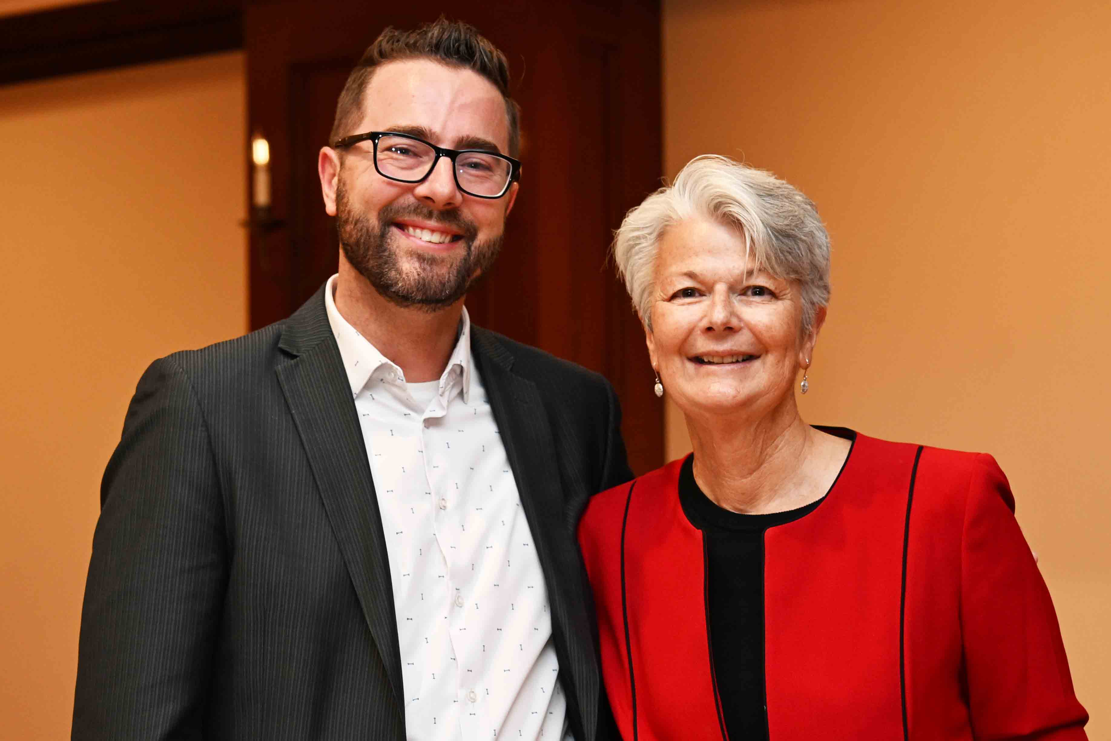 Two people smiling at an indoor event, standing side by side in formal attire.