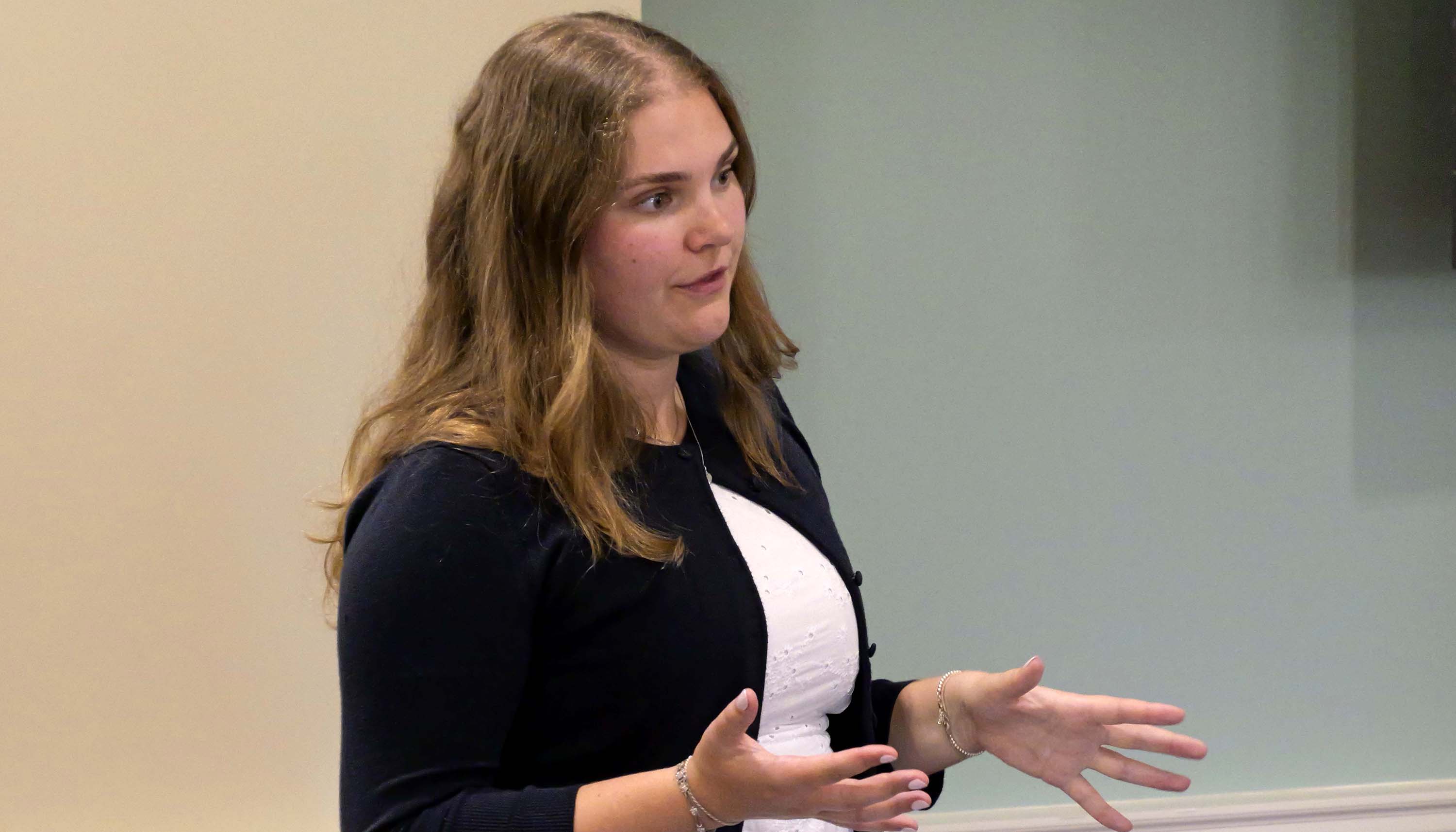 Woman speaking and gesturing with her hands during an indoor presentation.