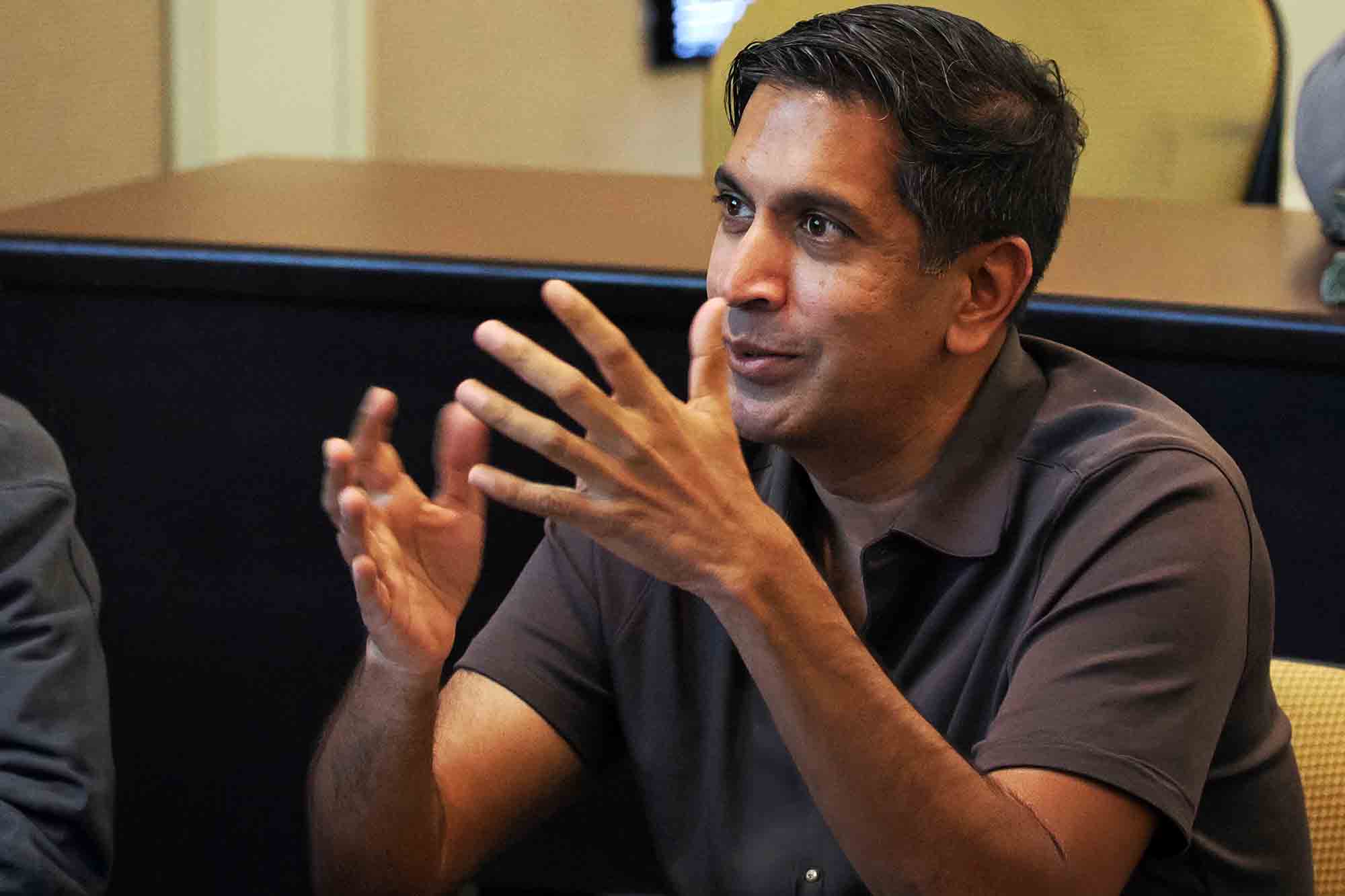 Man seated at a table gestures with both hands while speaking during a meeting or discussion.