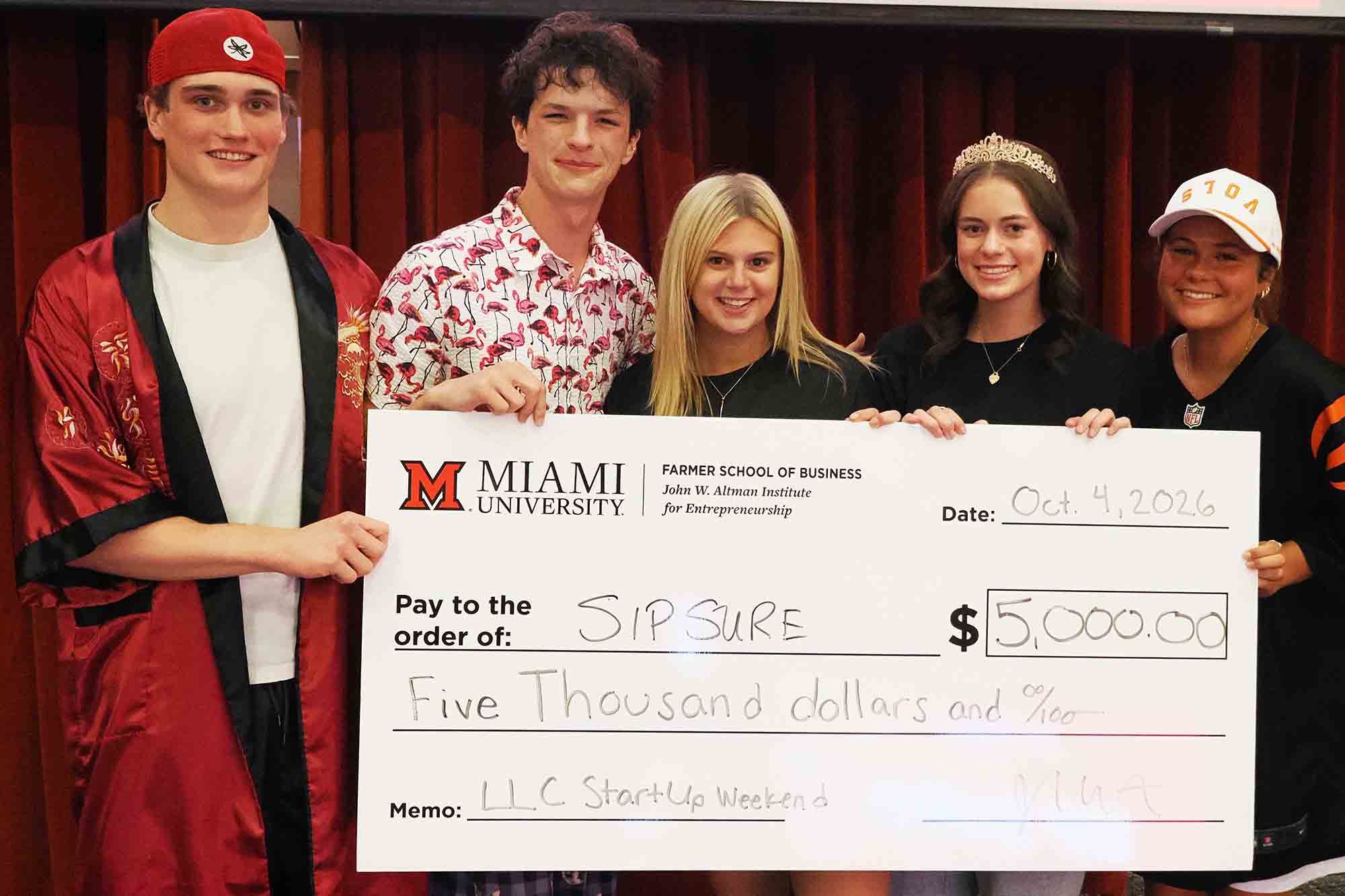 Five students pose indoors holding an oversized Miami University Farmer School of Business check for $5,000 made out to “SIPSURE.”