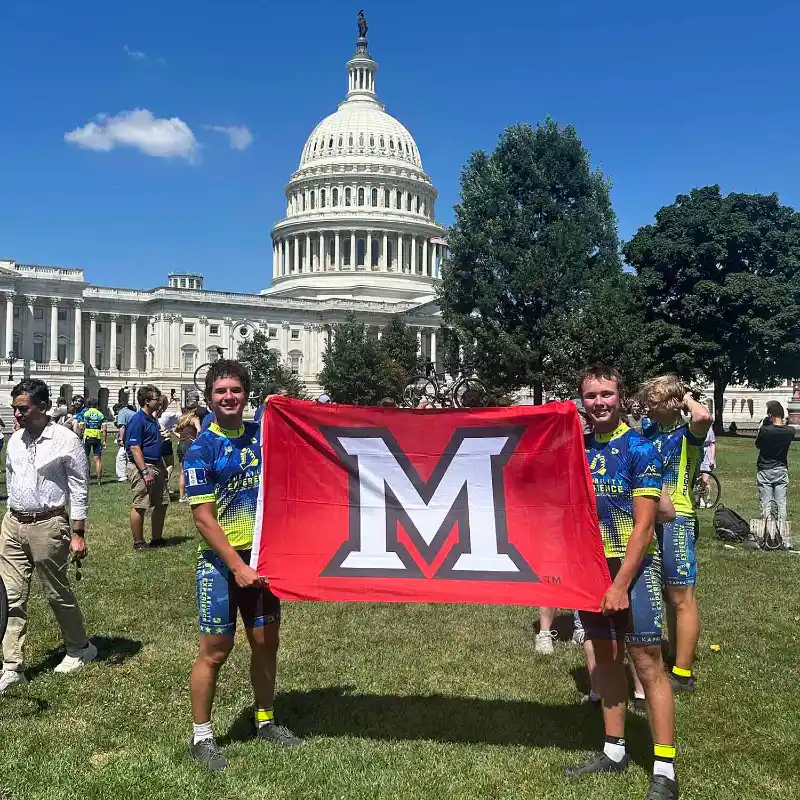  Charlie Taft  and Nick D’Angelo standing in front of capital building holding Miami flag