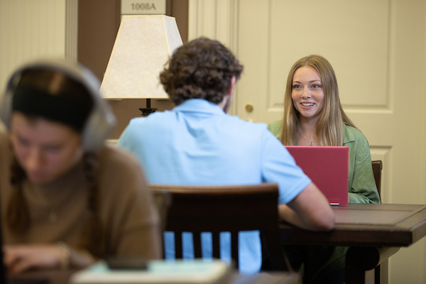 students  sitting at table together, with laptops, smiling, in lobby of farmer school of business