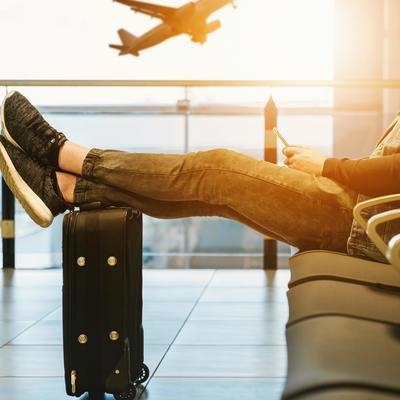 a plane takes off outside the airport lounge as a traveler rests his legs on a suitcase