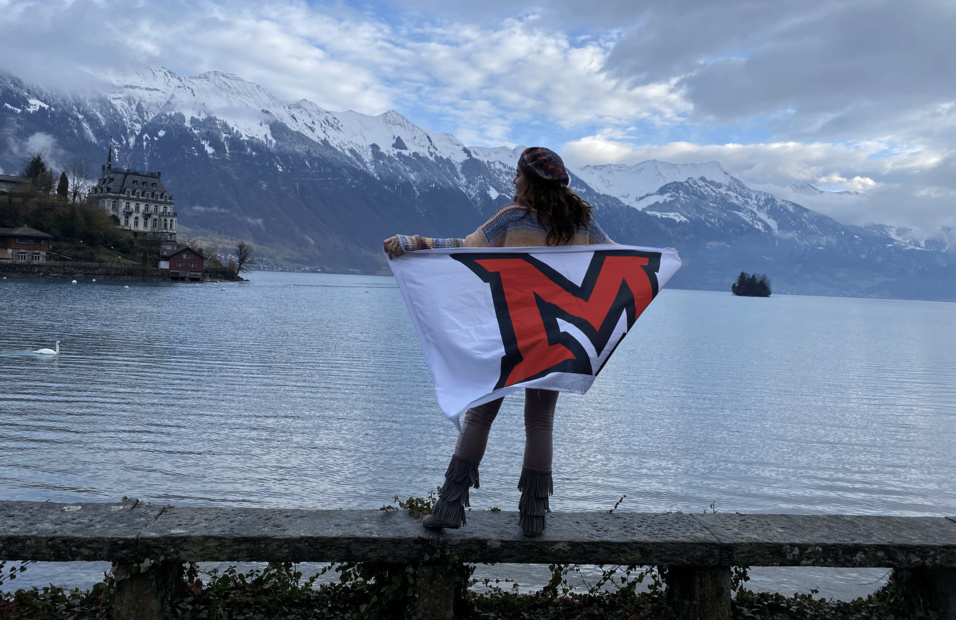 A student faces away from camera and wears a Miami M flag as a cape