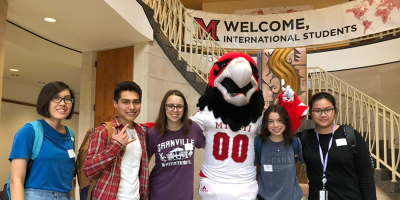 Students pose with Swooop in Armstrong Center. Sign in background reads 'Welcome international students'