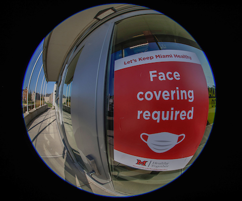 A fisheye mirror reflection of a sign reading face coverings required