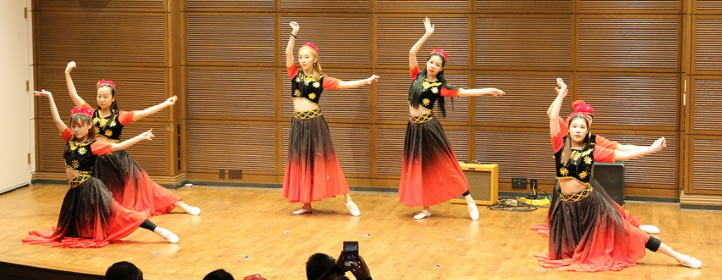 a group of students dance on stage wearing elaborate red and black dresses