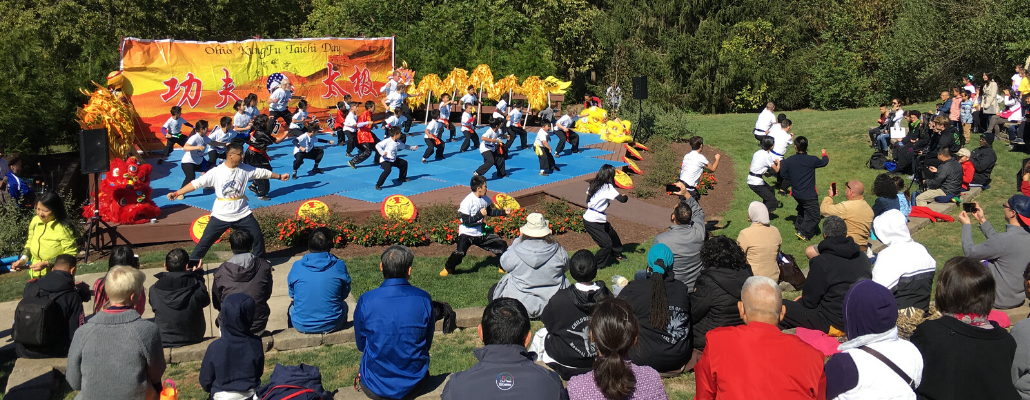people watch as a large group performs martial arts on an outdoor stage