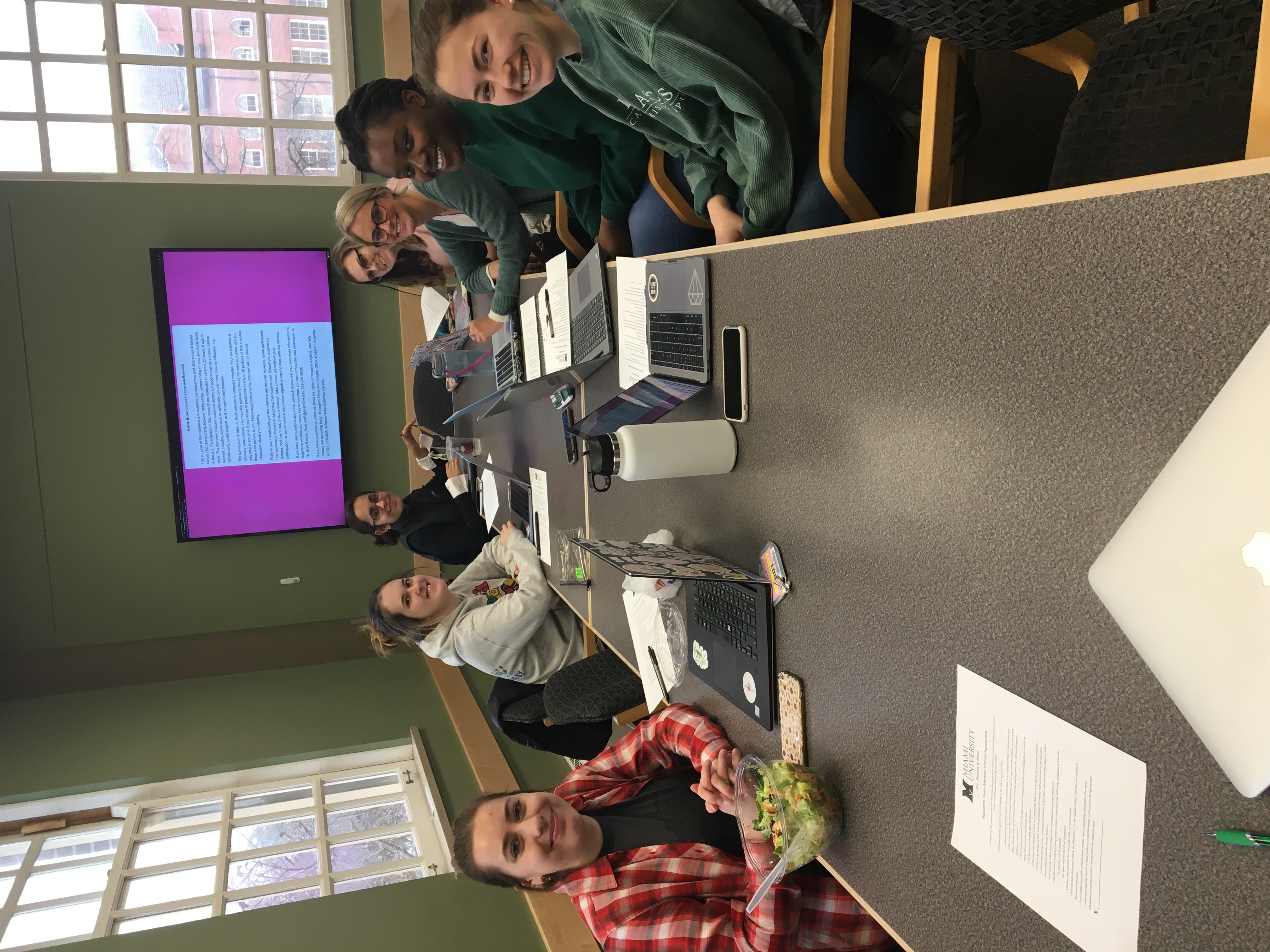 Students on Dr. Radina's team sit around a table near a screen