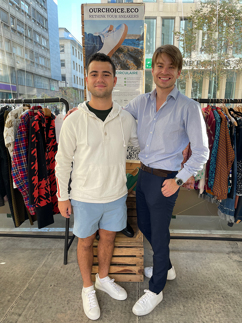 Max and friend pose in front of a rack of clothing