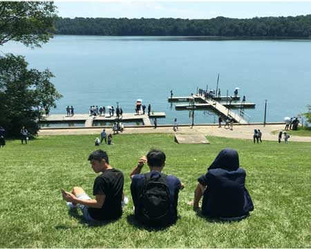Students sit on the grass and gaze out at the lake at Hueston Woods