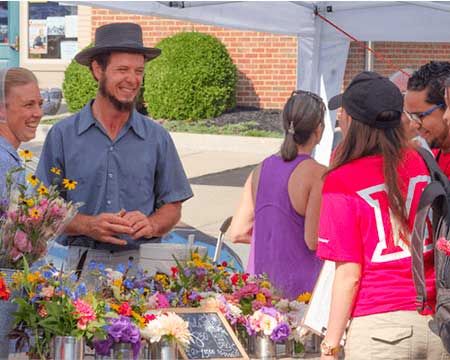 A farm couple smile at student shoppers as they tend their stand at the Uptown Farmers Market