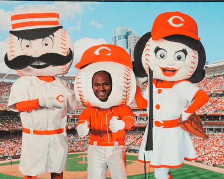 Reds mascots pose with a fan who is sticking his head through a mascot outline