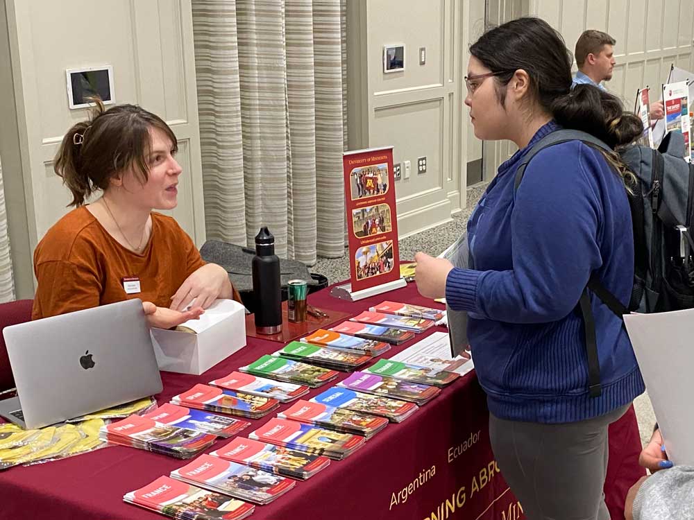 student speaking with staff member at a table with brochures for various countries